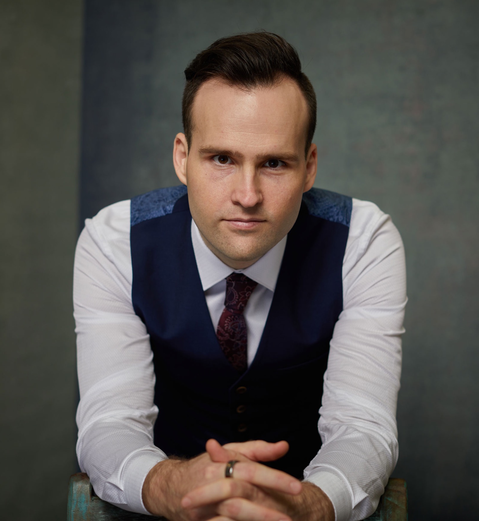 Andrew Ramsden in a waistcoat, leaning forward with his hands clasped, looking straight at the camera